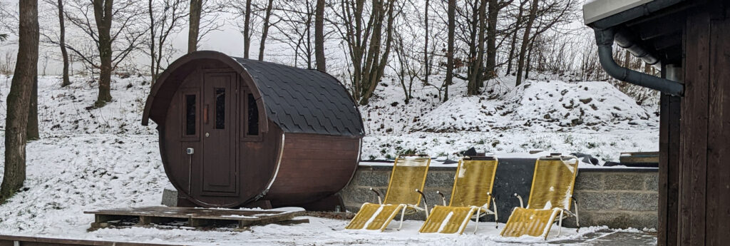 Fasssauna, daneben Liegestühle. Winterliche Atmosphäre mit Schnee.